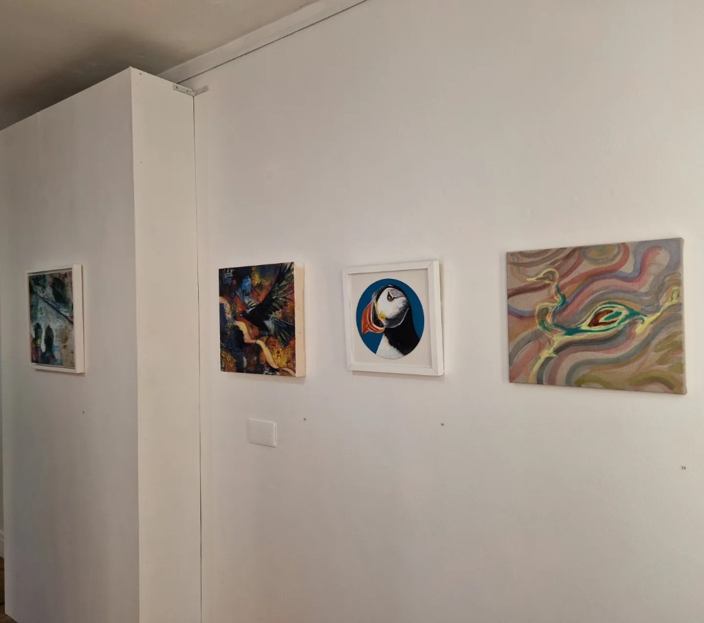 A wall of framed and unframed paintings in an exhibition setting.
