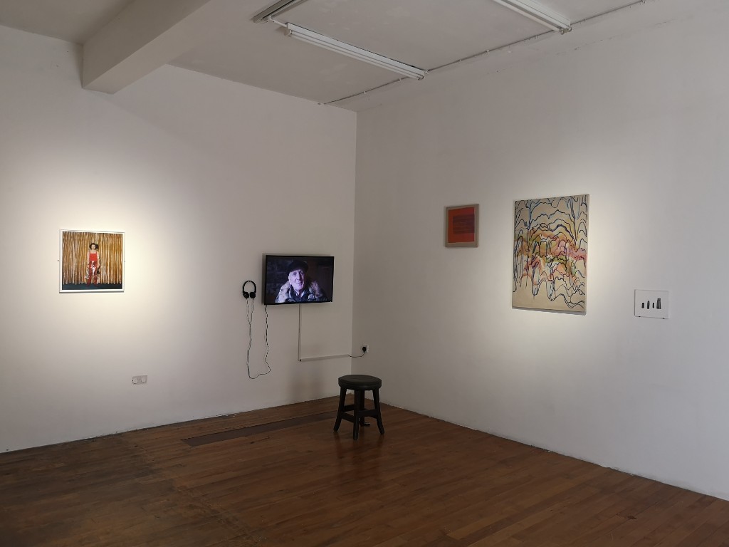 Gallery installation view including paintings and a video piece.