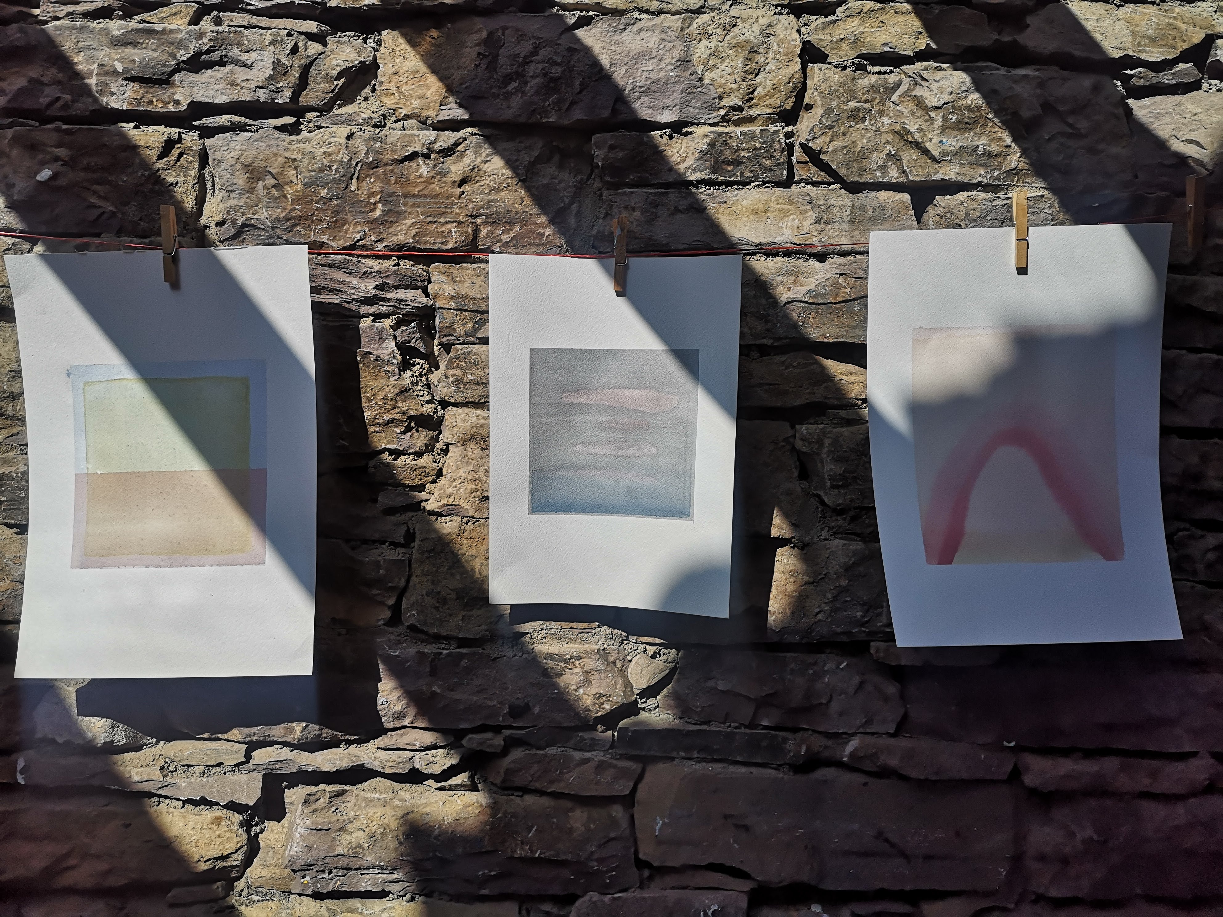 Three watercolours pegged to a line against a stone wall at Cill Rialaig, 2020.